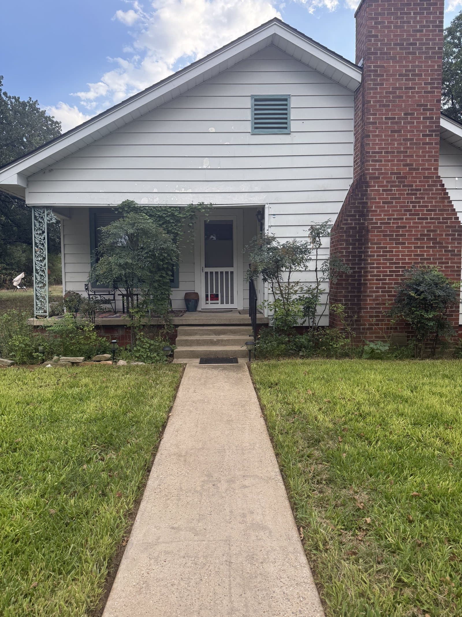 ROMAR House: a white clapboard country house with a red brick chimney and a vine-covered front porch, a concrete path leading up across the lawn.