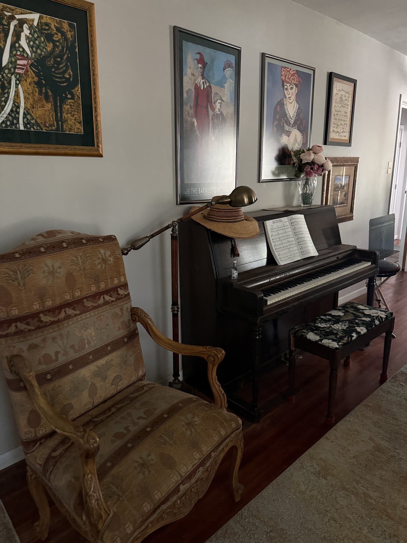 An upright piano with sheet music and a brass lamp beside an upholstered armchair at ROMAR House, beneath framed art.