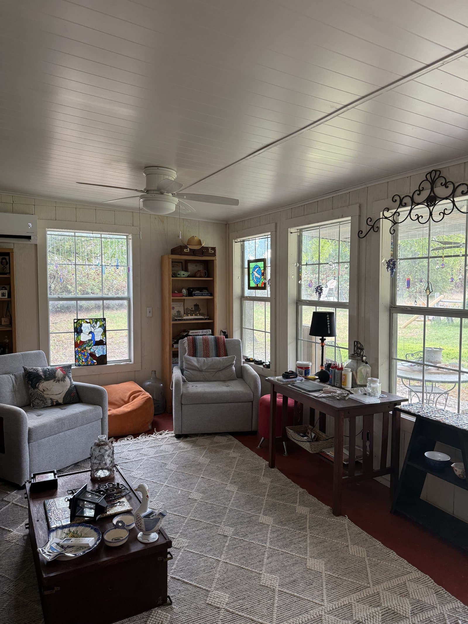The sun room at ROMAR House: windows on three sides with stained glass, two armchairs, a bookcase, a patterned rug and a writing desk with a lamp.